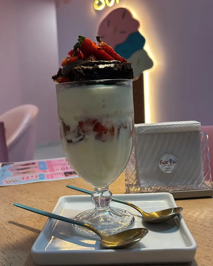 Antes: taça de sorvete com creme, morangos e brownie, fotografada no celular dentro da sorveteria